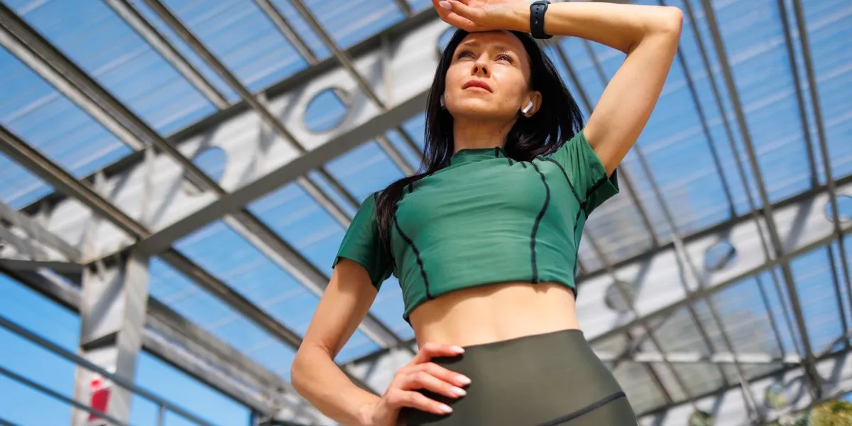 Femme s'entraînant en plein air avec un t-shirt technique vert, s'essuyant la sueur Femme s'entraînant en plein air avec un t-shirt technique vert, s'essuyant la sueur
